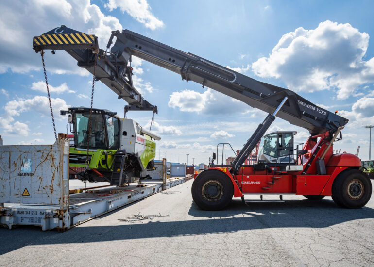 Ein Reachstacker hebt einen Mähdrescher auf einem offenen Container an